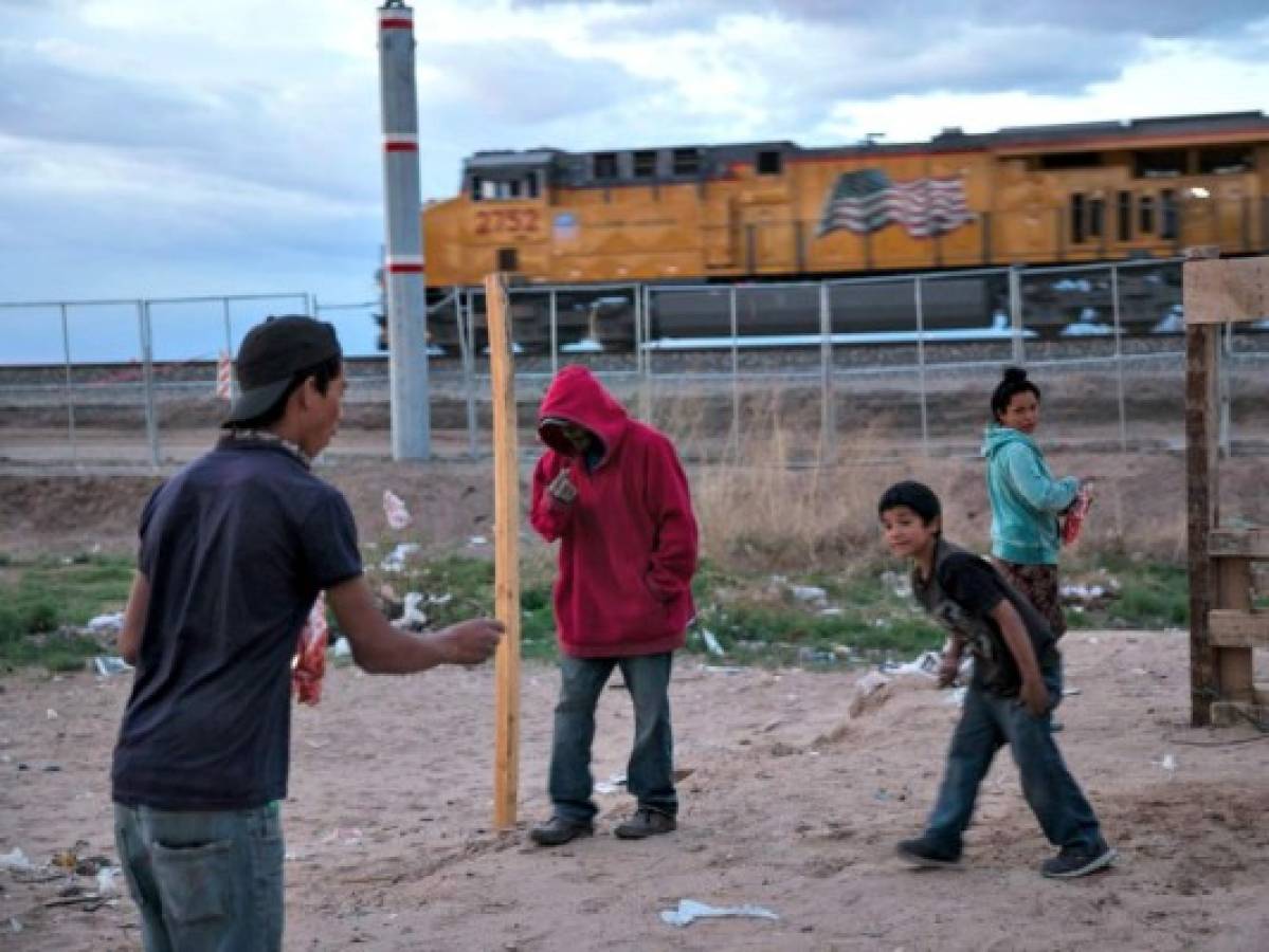 In this Wednesday, March 29, 2017 photo, children play a coin toss game in the sand as a train passes behind the fence marking the US-Mexico border, in the Anapra neighborhood of Ciudad Juarez, Mexico, across the border from Sunland Park, New Mexico. There are more than 650 miles of fence, wall and vehicle barriers along the nearly 2,000-mile border. (AP Photo/Rodrigo Abd)