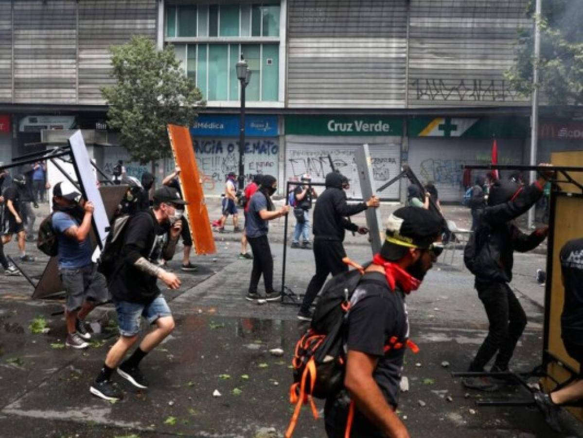 TOPSHOT - Demonstrators clash with riot police during a protest against Chilean President Sebastian Pinera's government in Santiago, on December 27, 2019. - Chile has been rocked by months of protests that began with strikes over metro fare hikes and quickly escalated into the most severe outbreak of social unrest since the end of the dictatorship of Augusto Pinochet nearly 30 years ago. (Photo by CLAUDIO REYES / AFP)