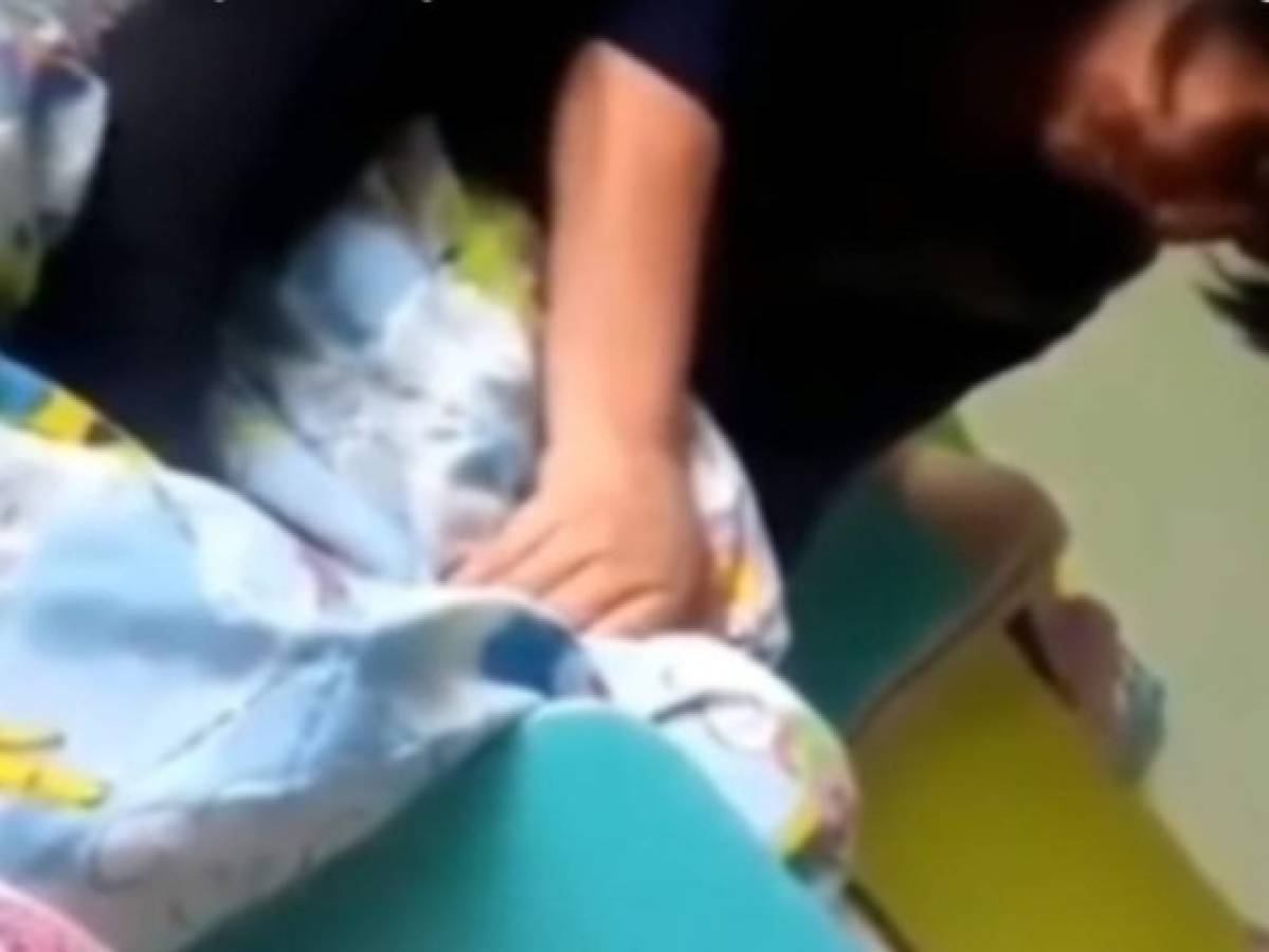 El material visual muestra cuando Umit Pirmajanova, de 50 años, cubre con una manta a un bebé que llora y le pone las manos en el cuello enfrente de otros niños.