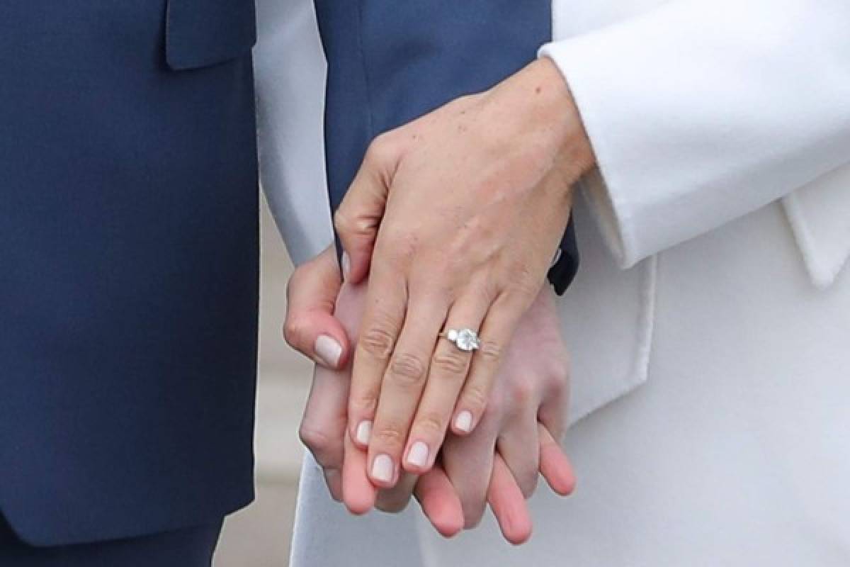 TOPSHOT - Britain's Prince Harry stands with his fiancée US actress Meghan Markle as she shows off her engagement ring whilst they pose for a photograph in the Sunken Garden at Kensington Palace in west London on November 27, 2017, following the announcement of their engagement.Britain's Prince Harry will marry his US actress girlfriend Meghan Markle early next year after the couple became engaged earlier this month, Clarence House announced on Monday. / AFP PHOTO / Daniel LEAL-OLIVAS