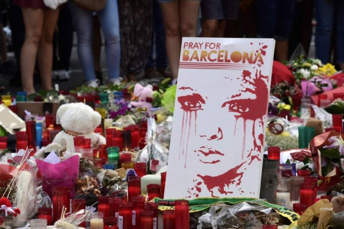 TOPSHOT - People stand next to flowers, candles and other items set up on the Las Ramblas boulevard in Barcelona as they pay tribute to the victims of the Barcelona attack, three days after a van ploughed into the crowd, killing 13 persons and injuring over 100 on August 20, 2017. Drivers have ploughed on August 17, 2017 into pedestrians in two quick-succession, separate attacks in Barcelona and another popular Spanish seaside city, leaving 14 people dead and injuring more than 100 others. In the first incident, which was claimed by the Islamic State group, a white van sped into a street packed full of tourists in central Barcelona on Thursday afternoon, knocking people out of the way and killing 13 in a scene of chaos and horror. Some eight hours later in Cambrils, a city 120 kilometres south of Barcelona, an Audi A3 car rammed into pedestrians, injuring six civilians -- one of them critical -- and a police officer, authorities said. / AFP PHOTO / JAVIER SORIANO