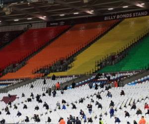 Los fanáticos se sientan socialmente distanciados mientras esperan el inicio antes del partido de fútbol de la Premier League inglesa entre West Ham United y Manchester United en el London Stadium. Foto: AFP.