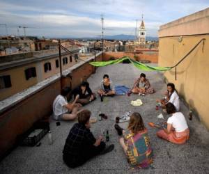 Un estudiante universitario comparte un aperitivo en la terraza de su edificio de apartamentos en el distrito de la Universidad de San Lorenzo, en el centro de Roma, durante el cierre del país destinado a frenar la propagación de la infección por COVID-19, causada por el nuevo coronavirus. Foto: Agencia AFP.