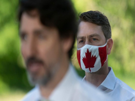 El parlamentario liberal William Amos, al fondo, utiliza una mascarilla que representa la bandera canadiense durante una conferencia de prensa del primer ministro Justin Trudeau en Chelsea, Quebec. (Adrian Wyld/The Canadian Press vía AP).
