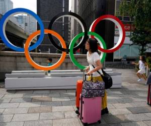 En esta foto del lunes 19 de agosto de 2019, turistas cargan sus valijas frente a anillos olímpicos en Tokio. (AP Foto/Jae C. Hong)