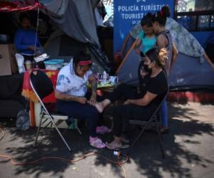 La migrante hondureña Valentina García, izquierda, le hace un pedicure a Elena Cruz, una migrante de El Salvador, el jueves 1 de julio de 2021 en un campamento de migrantes cerca del puente fronterizo peatonal El Chaparral, en Tijuana, México. (AP Foto/Emilio Espejel).