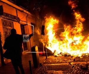 Un manifestante arroja basura a una barricada en llamas en Lavapiés, un vecindario de Madrid, España, el 15 de marzo de 2018. El centro de la capital española registró enfrentamientos por la muerte de un vendedor africano de 35 años que, según los testigos, murió mientras trataba de escapar de un operativo de la policía contra la venta ilegal callejera. (AP Foto/Alejandro Martínez Velez)