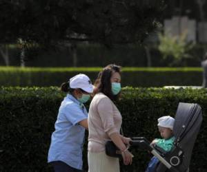Mujeres con mascarillas para protegerse del coronavirus empujan un carrito para niños en una calle de Beijing. Foto: Agencia AFP.