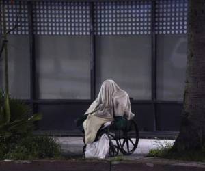 Una persona desamparada está sentada en una silla de ruedas bajo la lluvia en Sunset Blvd., en el barrio de Echo Park en Los Ángeles. Foto AP