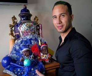 El inmigrante y peluquero venezolano Gustavo Acosta, de 36 años, seguidor de la religión yoruba, posa con un santuario yoruba en su departamento, el martes 9 de marzo de 2021, en Nueva York. (AP Foto/Kathy Willens)