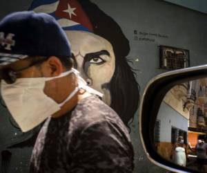 Un hombre con un cubreboca camina junto a un mural de Ernesto 'Che' Guevara, mientras otras personas se reflejan en el espejo de un carro en La Habana, Cuba, el martes 7 de abril de 2020. Foto: Agencia AP.