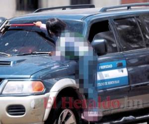 Esta niña es tan pequeña que no alcanza el vidrio de uno de los carros, por lo que tiene que subirse en un extremo de la llanta para poder llegar. Foto: El Heraldo