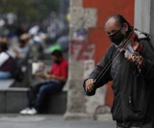 Fernando Castro, de 59 años, toca el violín para ganar propinas de gente que pasa caminando en Avenida Juárez en Ciudad de México el domingo 31 de mayo de 2020. (AP Foto/Rebecca Blackwell).