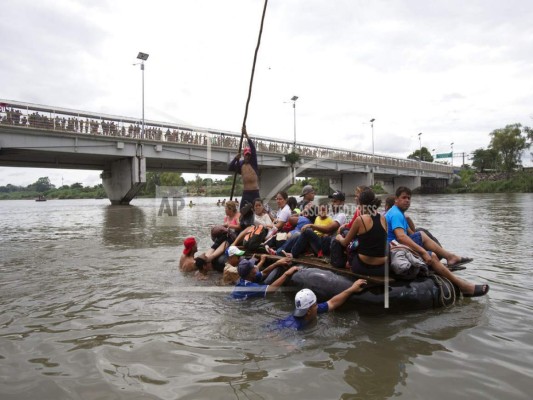 Un grupo de migrantes centroamericanos cruzan el río Suchiate a bordo de una balsa hecha con tubos interiores de tractores y tablones de madera, en la frontera entre Guatemala y México, en Ciudad Hidalgo, México, 20 de octubre de 2018. (AP Photo / Moises Castillo ).