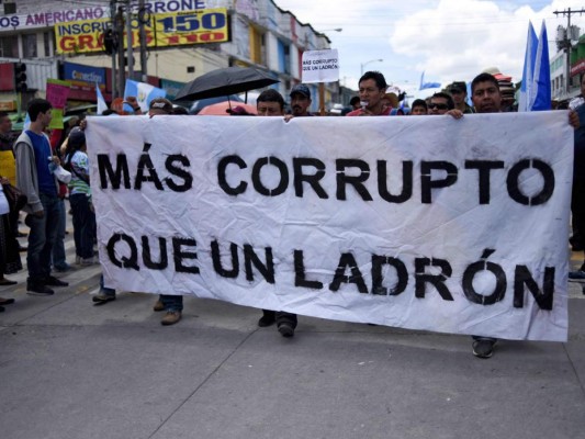 La gente sostiene una pancarta que dice 'Más corrupta que un ladrón' durante una visita a estudiantes universitarios para exigir la renuncia del presidente guatemalteco Jimmy Morales en Ciudad de Guatemala. Agencia AFP.