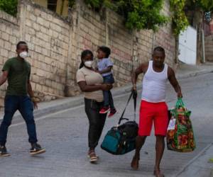 Jean Charles Celestin (derecha) carga con las pertenencias de su primo Jhon Celestin (izquierda), su esposa Delta De Leon y su hija Chloe, en Puerto Príncipe, Haití, el 22 de septiembre de 2021. Jhon Celestin llegó a la capital de Haití a bordo del último vuelo del día, Se había marchado tres años antes para buscar un empleo mejor pagado con el que mantener a su familia. (AP Foto/Joseph Odelyn)