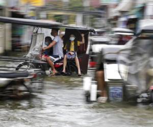 Los residentes que llevan máscaras para evitar la propagación del coronavirus se desplazan en motocicletas mientras transitan una carretera inundada debido al tifón Molave. Foto AP