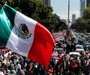 Una bandera mexicana ondea mientras cientos de taxistas se reúnen para protestar contra aplicaciones que ofrecen transporte en la Ciudad de México, el lunes 7 de octubre de 2019. Foto: AP.
