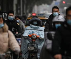 Viajeros vestidos con máscaras pasan por The Jade Boutique Hotel, donde los miembros del equipo de la Organización Mundial de la Salud (OMS) que investigan los orígenes de la pandemia del coronavirus covid-19 deben completar su cuarentena, en Wuhan, provincia central de Hubei en China, el 28 de enero. 2021. Foto: AFP