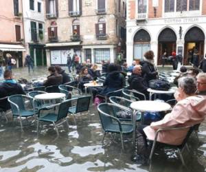 La vida continúa en medio de las inundaciones en Venecia y lugareños y turistas se sientan en un bar, en las mesas de la calle, a pesar de que el agua les sobrepasa los tobillos el 17 de noviembre del 2019. Foto: AP.