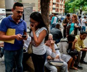 Los venezolanos leían los requisitos para una 'Visa de Responsabilidad Democrática' en sus teléfonos celulares, luego de tomar fotografías de la lista que se exhibe afuera del Consulado de Chile en Caracas. foto AFP