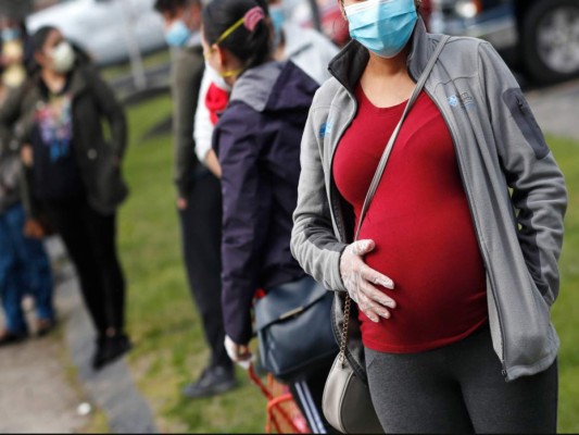 Una mujer embarazada provista de mascarilla y guantes hace fila para recibir una despensa de alimentos de Healthy Waltham durante la pandemia de COVID-19, afuera de la iglesia de St. Mary, en Waltham, Massachusetts. (AP Foto/Charles Krupa).