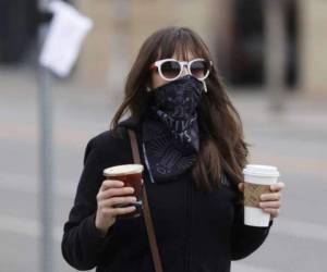 Una mujer con tapabocas lleva dos cafés que acaba de comprar en una cafetería de Denver, que lentamiente empieza a reabrir sus negocios. Foto AP