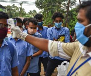 Niños con mascarillas se desinfectan las manos y pasan un control de temperatura corporal a su llegada para un examen escolar durante la pandemia del coronavirus en Kochi, estado de Kerala, India. Foto: AP.