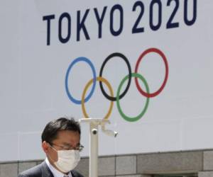 Un hombre con una mascarilla pasa junto a un cartel anunciando los Juegos Olímpicos de Tokio del 2020 en la capital japonesa el 25 de marzo del 2020. Foto: Agencia AP.