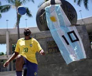 Marcio Pereira, de 57 años y quien se hace apodar 'Pelé', domina el balón junto a un monumento adornado con una bandera argentina y con el 10 de Diego Maradona frente al estadio Maracaná en Río de Janeiro. (AP Foto/Silvia Izquierdo)