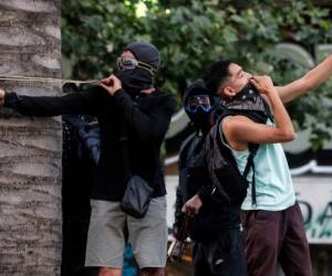 En esta foto de archivo tomada el 06 de noviembre de 2019, un manifestante se hace una a sí mismo mientras otro usa una honda contra la policía antidisturbios durante una protesta contra las políticas económicas del gobierno en Santiago. Foto AFP