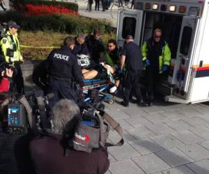 Policías auxilian a socorristas a trasladar a un centro médico a un militar que resultó herido en el tiroteo al Parlamento de Canadá.