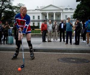 Los turistas observan a un hombre que usa una máscara del presidente estadounidense Donald Trump y una camiseta rusa de hockey que realiza una protesta frente a la Casa Blanca en momentos en que se confirmó la primera acusación por el caso ruso. (Foto: AFP/ El Heraldo Honduras/ Noticias Honduras hoy)