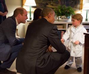 El príncipe George utilizando una bata blanca mientras saluda al expresidente de los Estados Unidos, Barack Obama.