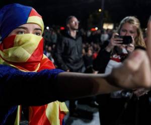 Una mujer, cuyo rostro está cubierto con una bandera catalana pro-independencia, gesticula mientras la gente se reúne en la Plaza Catalunya de Barcelona esperando los resultados de un referéndum de independencia prohibido tras el cierre de las mesas de votación el 1 de octubre de 2017. mientras se movían para detener el referéndum de independencia de Cataluña después de que fuera prohibido por el gobierno central en Madrid. Al menos 92 personas resultaron heridas mientras cientos intentaban evitar que se cerraran las mesas de votación, dijeron funcionarios catalanes. / AFP / CESAR MANSO