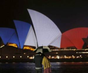 Una pareja se cubre de la lluvia en Sidney (Australia). Al fondo, la Ópera de Sidney alumbrada con los colores nacionales de Francia, en solidaridad con los atentados que han costado la vida a 127 personas en París.