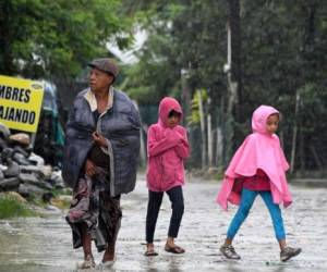 Una mujer y dos niñas caminan bajo la lluvia en el municipio de Omoa, a unos 210 km al noroeste de Tegucigalpa, el 11 de noviembre de 2017.La temporada de lluvias en Honduras, que va de abril a noviembre, ha causado la muerte de al menos 43 personas. / AFP PHOTO / Orlando SIERRA