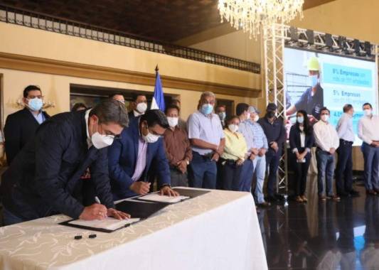 El presidente Hernández y el ministro de Trabajo, Olvin Villalobos, mientras firman el acuerdo del salario mínimo. Foto: Cortesía.
