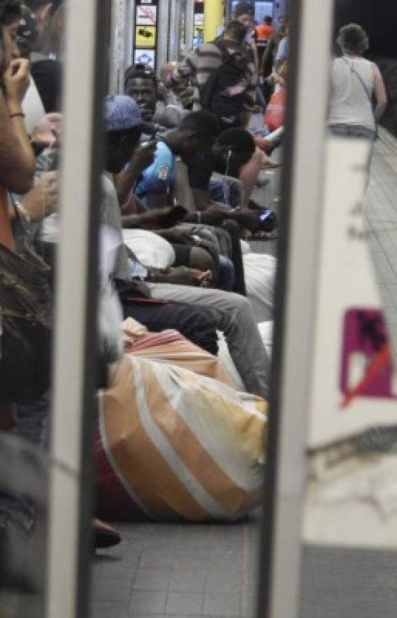 Hombres africanos con sus mantas cargadas de mercancía esperan el metro para cambiar de punto de venta en Barcelona. Venden productos de lujo falsificado, en lo que se conoce como “top manta”.
