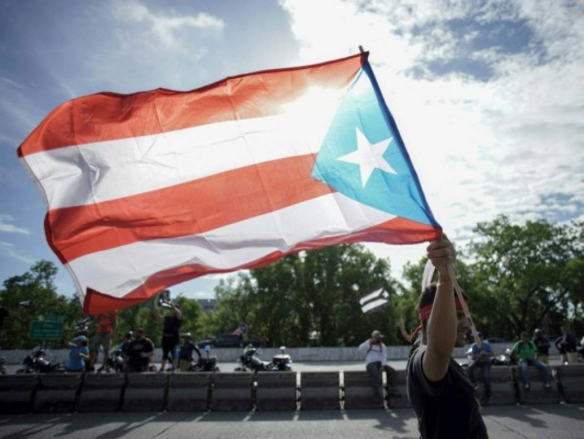 Un manifestante ondea la bandera puertorriqueña en San Juan, Puerto Rico, el día 9 de las continuas protestas en las que se exige la renuncia del gobernador Ricardo Rosselló. Foto: Agencia AFP.