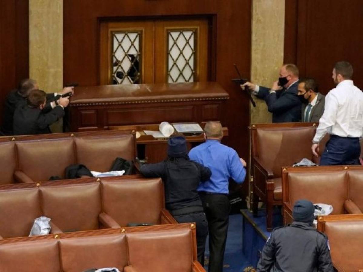 Los oficiales de policía del Capitolio apuntan con sus armas a una puerta que fue vandalizada en la Cámara de la Cámara durante una sesión conjunta del Congreso el 6 de enero de 2021 en Washington. Foto: AFP