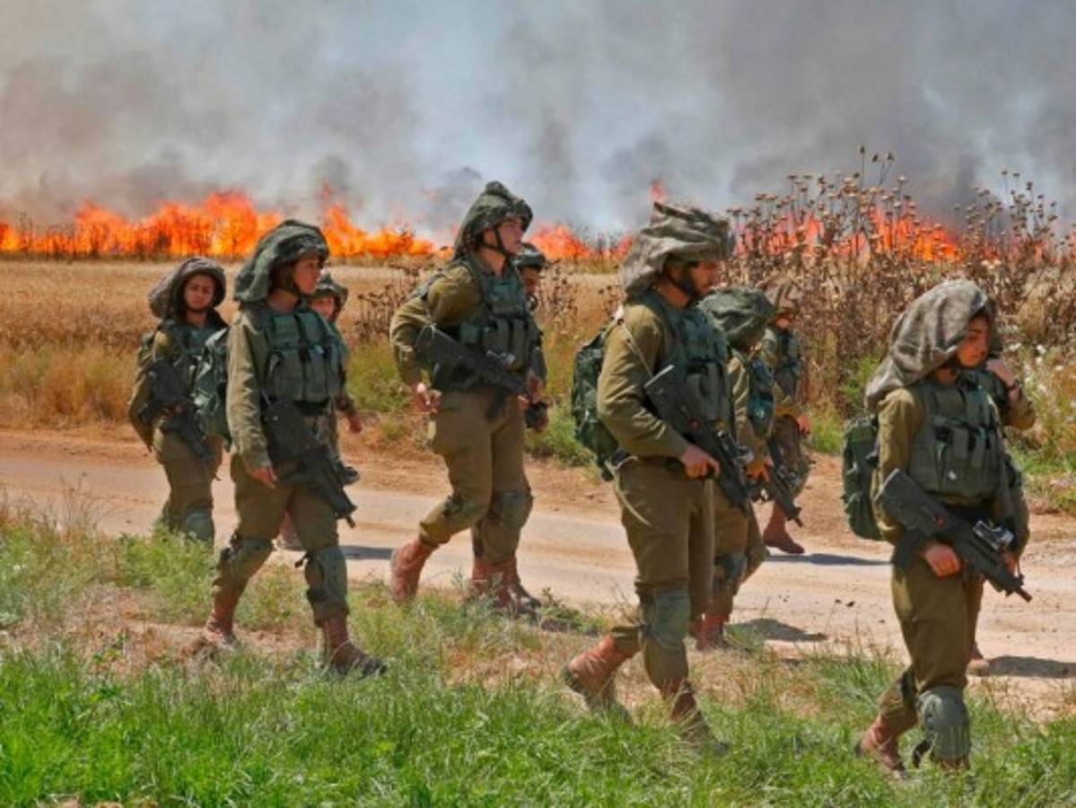 Palestinians in the smoke billowing from burning tyres look at clashes with Israeli forces near the border between the Gaza strip and Israel east of Gaza City on May 14, 2018, as Palestinians protest over the inauguration of the US embassy following its controversial move to Jerusalem.Dozens of Palestinians were killed by Israeli fire on May 14 as tens of thousands protested and clashes erupted along the Gaza border against the US transfer of its embassy to Jerusalem, after months of global outcry, Palestinian anger and exuberant praise from Israelis over President Donald Trump's decision tossing aside decades of precedent. / AFP PHOTO / MAHMUD HAMS