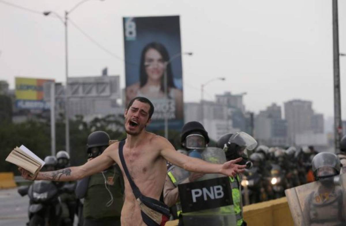 Un manifestante anti-gobierno sostiene una Biblia bajo vigilancia de la policía antidisturbios durante una marcha en Caracas, Venezuela. Foto: Agencia AP.