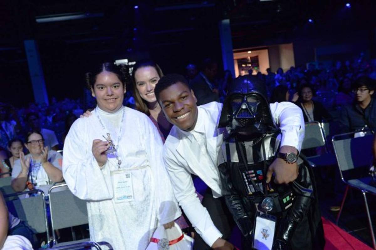 This photo provided by Disney Enterprises shows co-stars John Boyega, right, and Daisy Ridley, rear, of Star Wars The Force Awakens giving away their Disney Infinity 3.0 Edition character figures, Finn and Rey, to two lucky fans during the video games presentation at the D23 Expo on Sunday, April 16, 2015, in Anaheim, Calif. (Disney Enterprises, Inc. via AP)