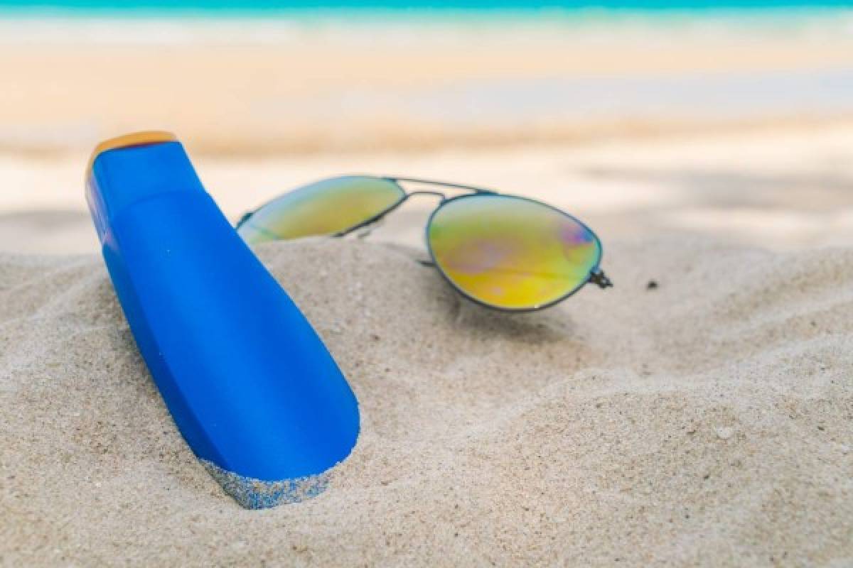 Sunglasses and sun cream on white sand beach