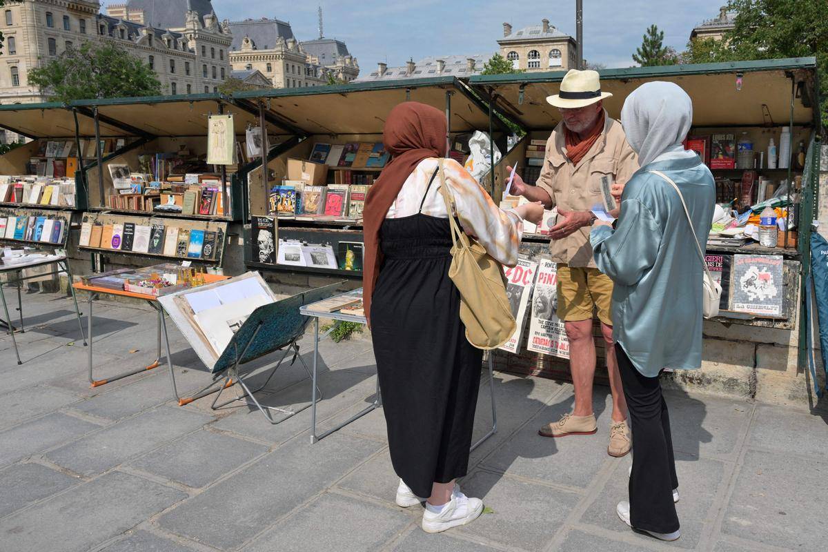 $!Un bouquiniste habla con clientes en París. Cajas de madera verde que tienen siglos de antigüedad albergan sus libros.