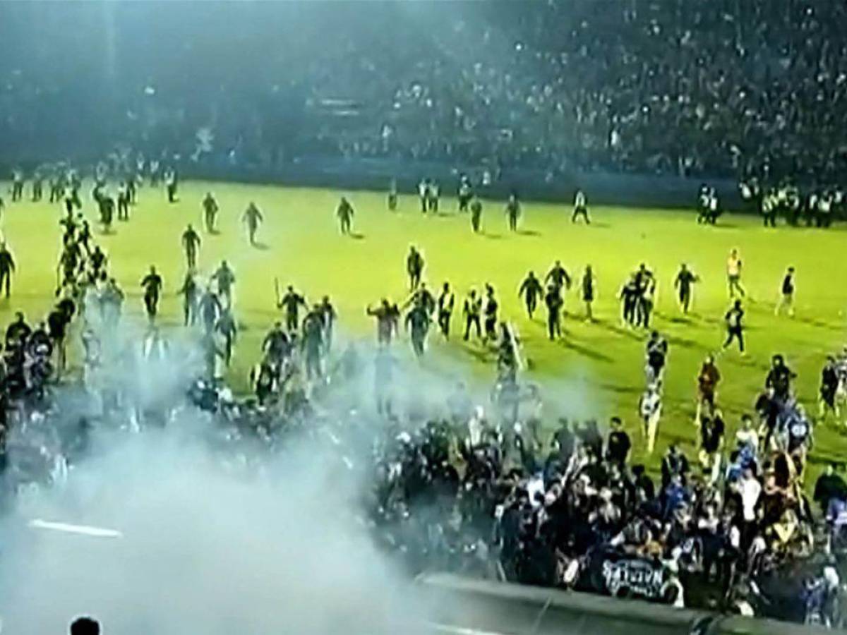 Esta captura de pantalla de un video de AFPTV tomado el 1 de octubre de 2022 muestra gases lacrimógenos en la multitud mientras la gente corre en el campo después de un partido de fútbol.