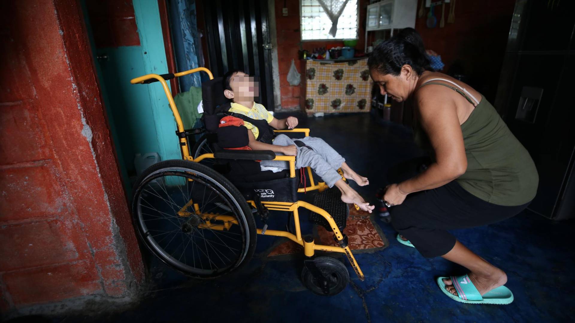$!Ángel sentado en una silla de ruedas que le donaron, mientras su madre le coloca los zapatos. El pequeño tiene 6 años.