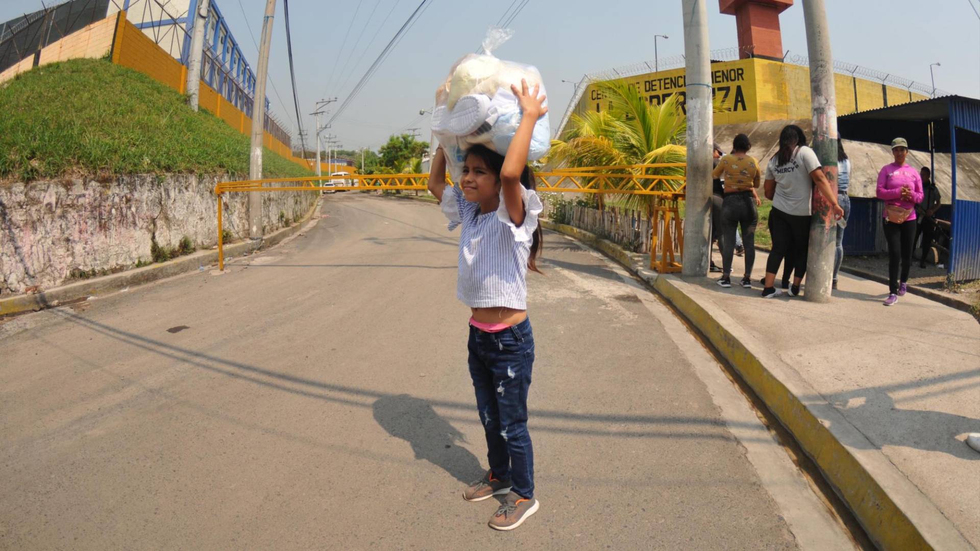 $!Esta niña salvadoreña carga sobre su cabeza uno de los paquetes con ropa y alimentos que espera pueda llegar a manos de papá, que está privado de libertad en la cárcel de Mariona.