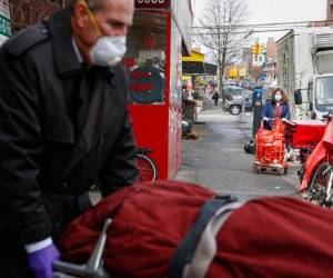El gerente de la firma publicitaria ABC Displays, Rodolfo Gómez, en el fondo al centro, y sus empleados muestran en su empresa una caja de cartón que puede servir de cama de hospital y féretro si el paciente fallece, en Bogotá, Colombia. Todos portan mascarillas para protegerse de la pandemia del coronavirus. (AP Foto/Fernando Vergara)